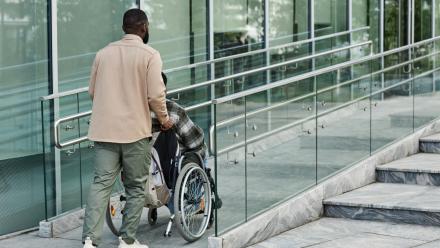 Man pushing a person in a wheelchair up a ramp